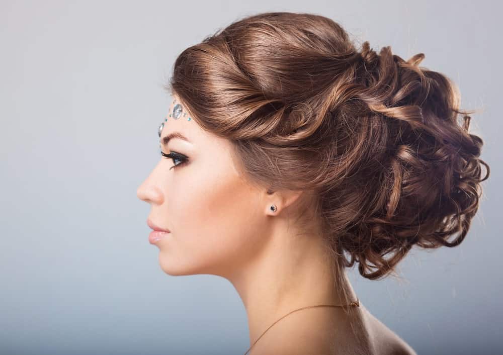 Feeling a little fancy? Go for this stylish braided bun style. The hairstyle features long brunette hair tied in a messy bun at the back of the head. In the front, the hair is tucked to the side. The same strands eventually end up in the bun. If you want to show off your earrings, this hairstyle is probably what you are looking for. 
