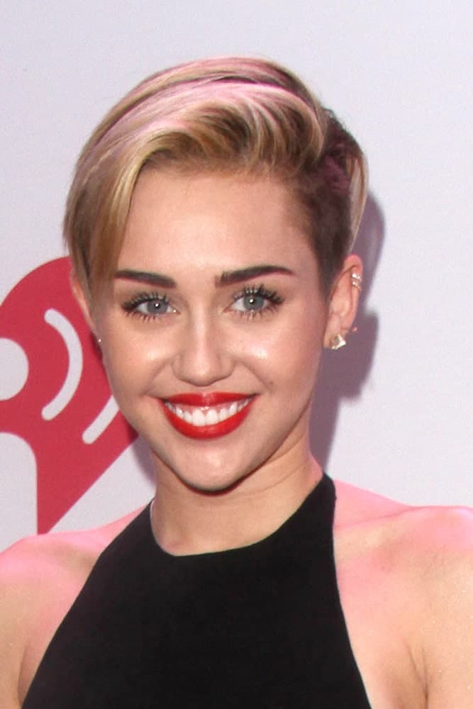 Miley Cyrus started the trend of sweeping your hair in one swoop onto the side. She looks absolutely stunning with the red lipstick, long lashes, and thick eyebrows. 