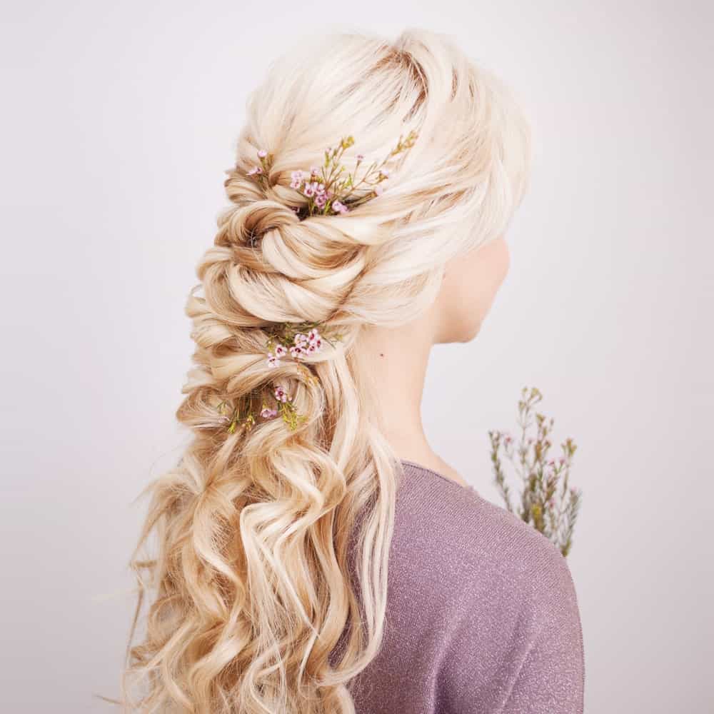 Nothing says elegance like this hairstyle for long and blonde curly hair. It features hair cut in layers and gathered at the back of the head where the top layer forms a loose half-braid. The rest of the hair simply flows down the shoulders and over the back. In the front, side bangs perfectly frame the face to bring out the eyes. This hairstyle gives you a lot of options for decorating your hair. Whether you put in flowers of some fancy clips, you are bound to look stunning. The cherry on top – you won’t have to worry about loose strands going into your eyes when you rock this hairstyle. 