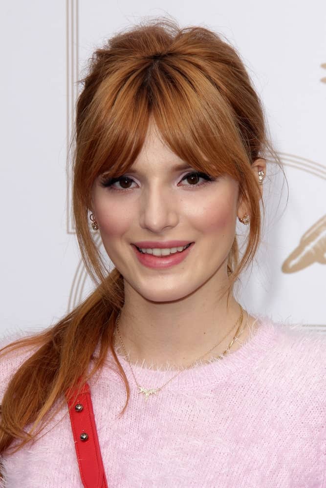 Bella Thorne could not look anymore lovelier than this! She is sporting long hair tied in a pony and heavy front bangs parted in the middle. While the short bangs cover most of the forehead, her face is framed by the chin-length layers. To complete the look, the ponytail is casually thrown to the front on one side.