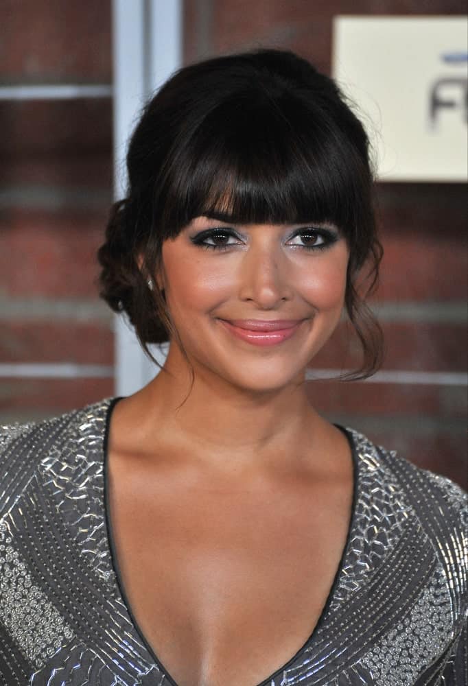 Check out the stunning look of Hannah Simone. The hairstyle features straight cut blunt bangs. The hair is loosely tied in a bun at the back while a few loose, slightly curly strands of hair frame the face from both sides to complete the look. If you are aiming for a soft, lovely look, this is the hairstyle for you! 