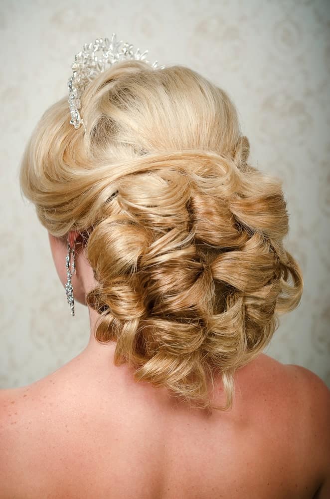 Want to feel a little fancy? Go for the ultimate princess look with this hairstyle! It features long blonde hair. This hairstyle works best when your hair has a loose curly texture. It gathers your hair at the back in a loose bun. However, as you can see, it is no ordinary bun! The strands of your blonde hair need to go around in loops to create this beautiful look. In the end, slay the look by adding a tiara. With this hairstyle, you can be the queen that you are! Do keep in mind that while this hairstyle offers a classic bridal look, it is equally good for prom night, date nights, or any other formal event!