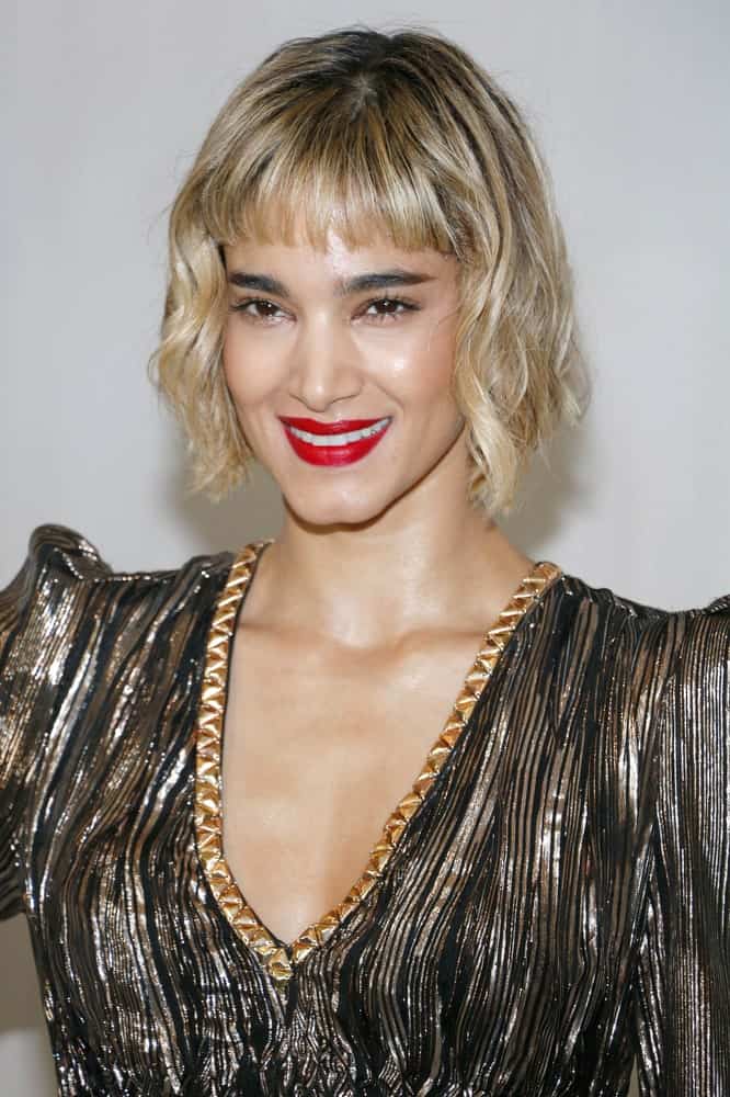 Looking for a new, stylish look to go with your short blunt bangs? Go for curly, tousled hair! Modeled by Sofia Boutella, this hairstyle features short blunt bangs, covering only half of the forehead. The bangs are coupled with chin-length curly hair. Whether you carry an ordinary straight bob or go for an asymmetrical bob, blunt bangs look good with all! 