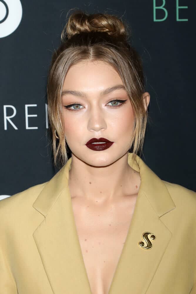 Gigi Hadid's light brown hair styled into a small sock bun with her mid-length bangs parted at the center, framing her face effectively.