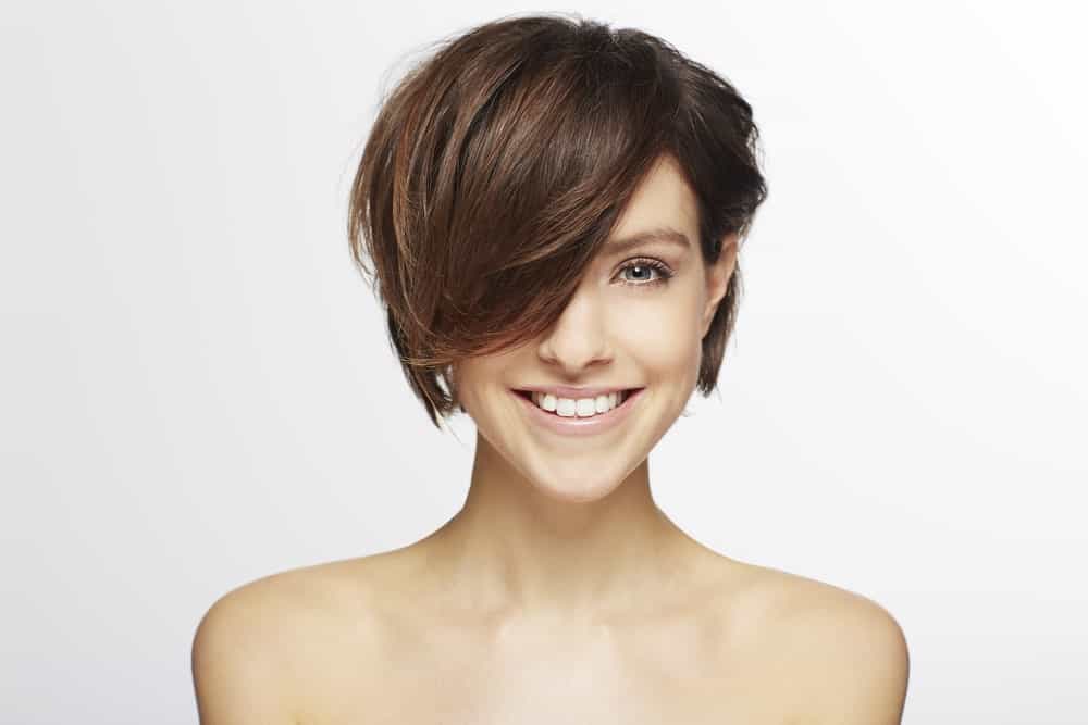 This is a super chic and unique hairstyle that is similar to a pixie-cut, except that a thick, sleek lock of hair is falling on the face on one side and from the other side; the hair has been pinned behind the ear.
