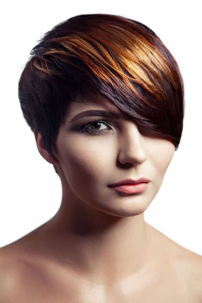For a style that’s loaded with beauty and grace, consider this short hairstyle with highlights. A pixie cut combined with extra deep, eye-skimming bangs swept to a side, this style also adds luster and shine with the bright amber honey streaks at the top.