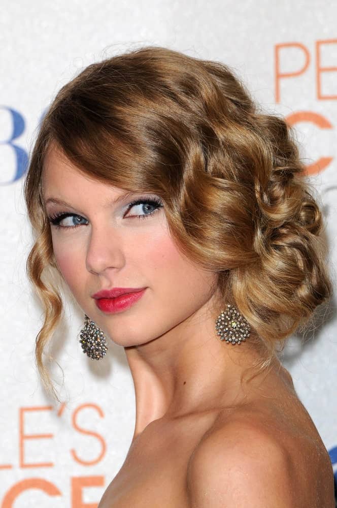 Taylor Swift’s sophisticated wedding hairstyle is swift and easy to recreate because all it requires is a bit of excessive curling before twirling the tousled strands into a loose low bun at the side. Let a sole strand hanging on the other side to balance the one-sided bunch.