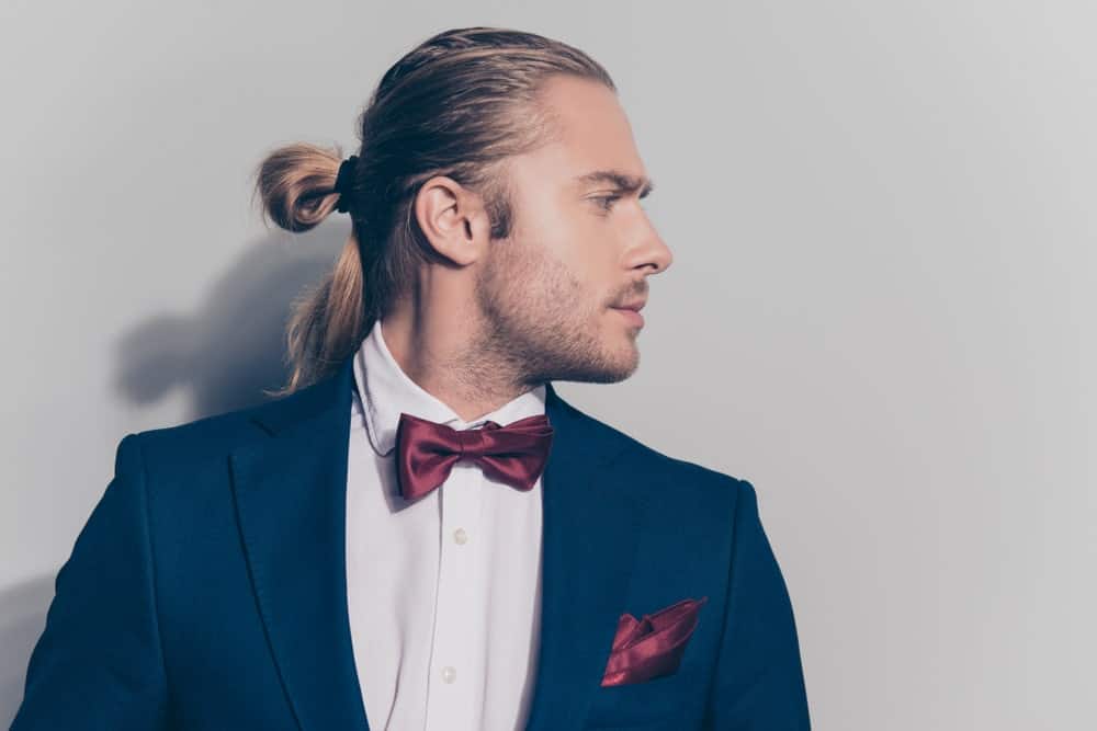 Do you know you can rock a man bun with a tuxedo? Just check out this great style. This model has his long hair slicked back from his forehead and tied back in a half man bun. Note that only the front of his hair is gelled back. The hair in his ponytail and down his back has minimal product, which gives this style balance and keeps thing both casual and sophisticated at the same time.