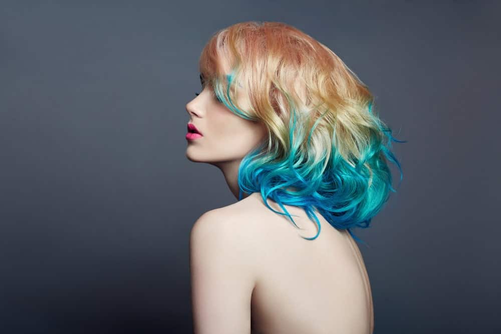 This mermaid-style hair look shows off a variety of jewel-blue colors, including shades of bright turquoise and sapphire. Although most of the color is situated on the bottom half of her hair, tendrils of the blue color have bled up. The model’s hair has been given further dimension by coloring her roots a strawberry blonde, which graduates to a lighter blonde before it meets the blue. 