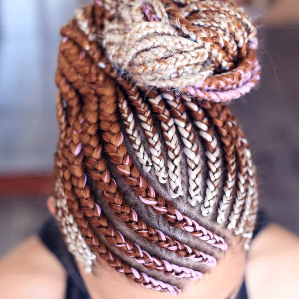As the lady in the picture shows, you don’t need to keep your long braids dangling all the time. She looped her long, dangling braids into a twisted bun onto the back and top of her head. To make the look even more dramatic, she incorporated brown-auburn, pale gold, and candy-pink threads into her hair to make her look stand out.