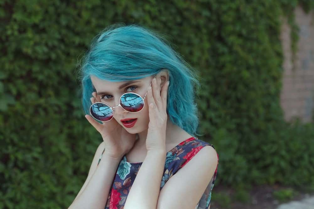 Woman with blue hair looking over her sunglasses.