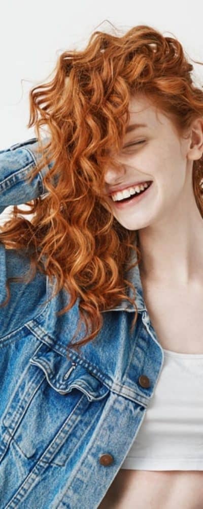 A red-haired girl smiles and touches her curls on a white background