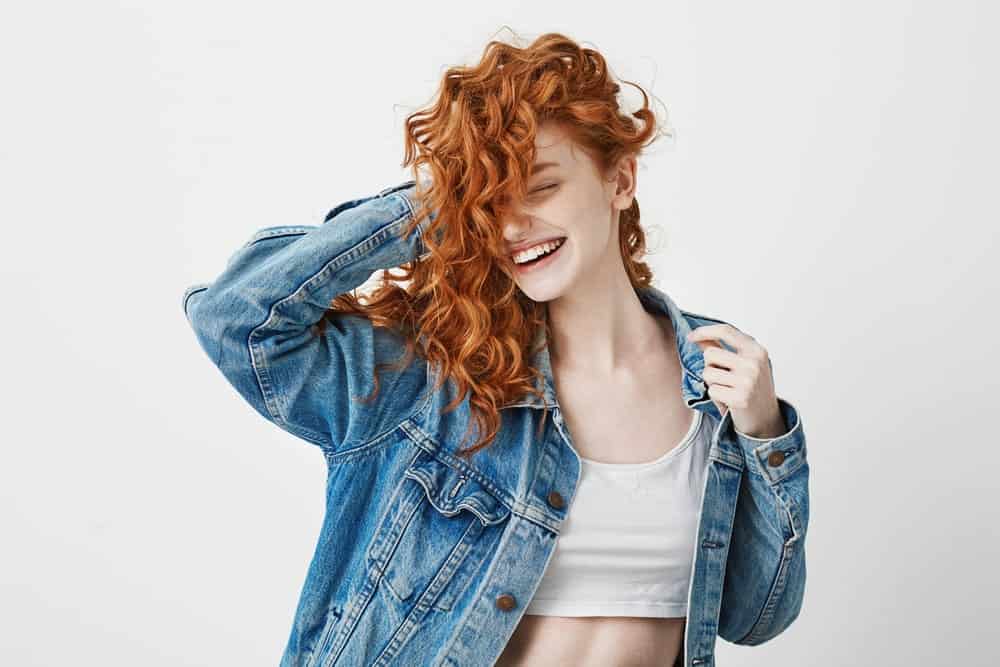 A red-haired girl smiles and touches her curls on a white background