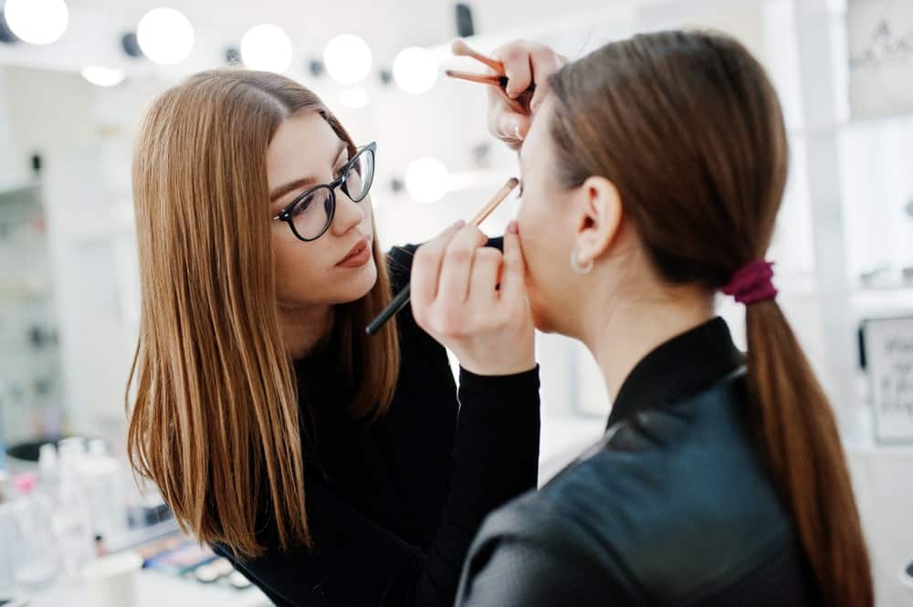 A makeup artist applies eyeshadow on a woman.