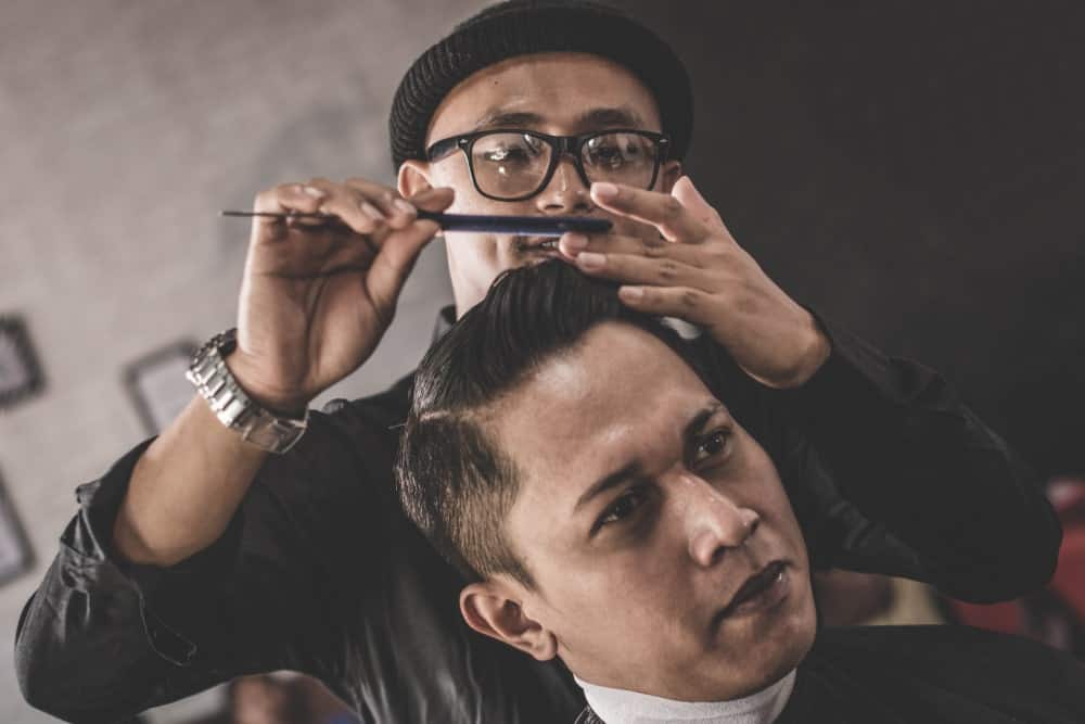 Barber styling man's hair with pomade and a comb.