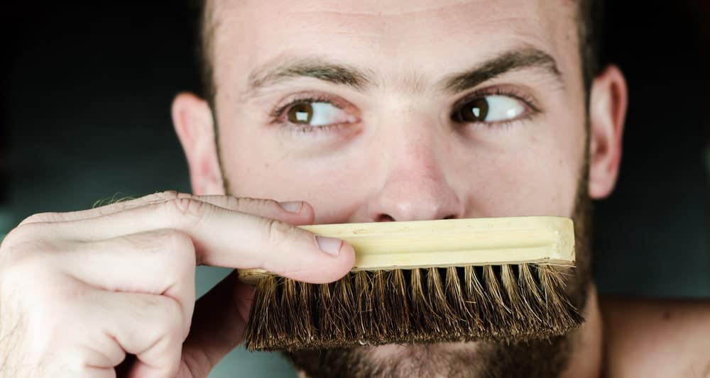 A close up shot of this man looking sideways and covering his mouth with a beard brush.