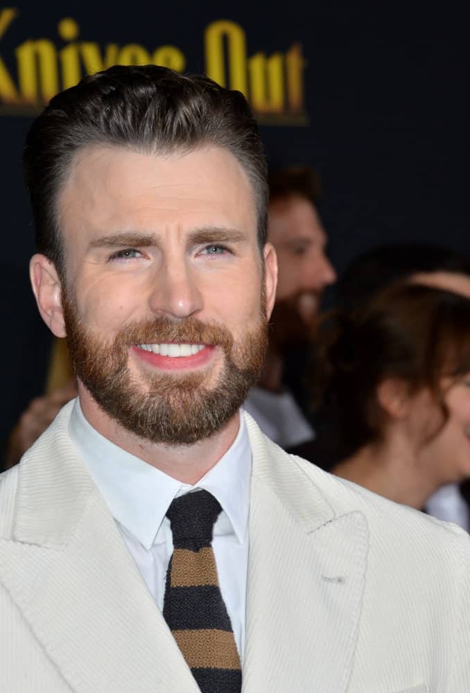 On November 15, 2019, Chris Evans attended the premiere of "Knives Out" at the Regency Village Theatre. He paired his vintage white suit with a scruffy beard and a brushed back pompadour hairstyle.