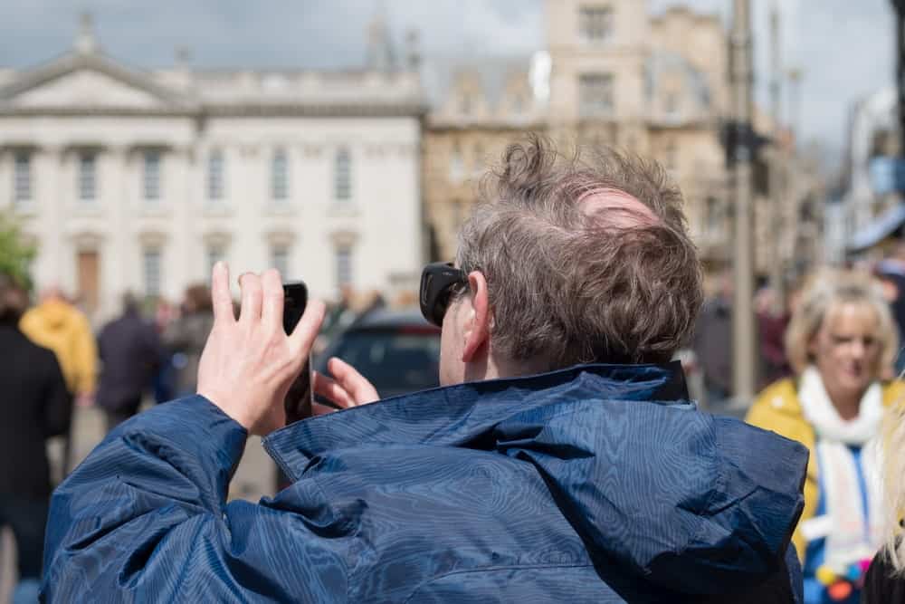 A comb over hairstyle of a man in a navy blue jacket, taking a photo in Cambridge, UK.