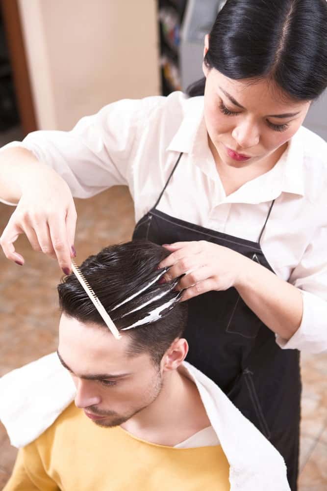 Hairdresser styling man's hair with a comb and mousse.