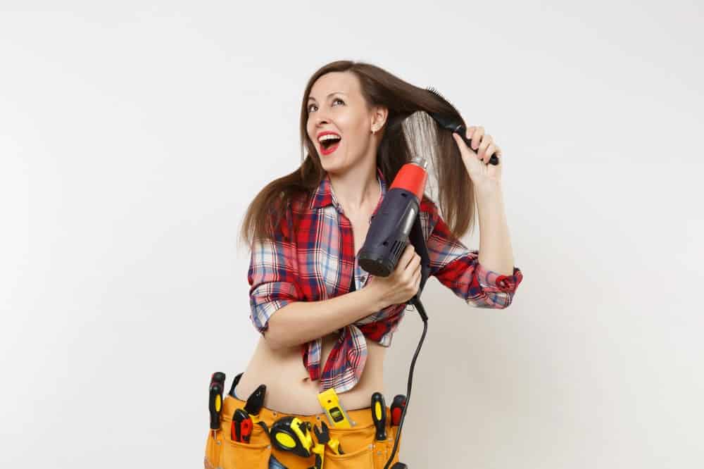Heat Gun Vs Hair Dryer. A woman using a heat gun on her hair.
