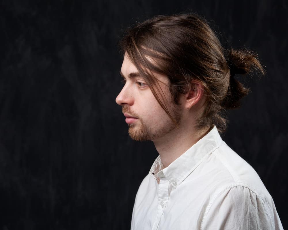 Side profile of a young man with mustache, fringe and a ponytail.
