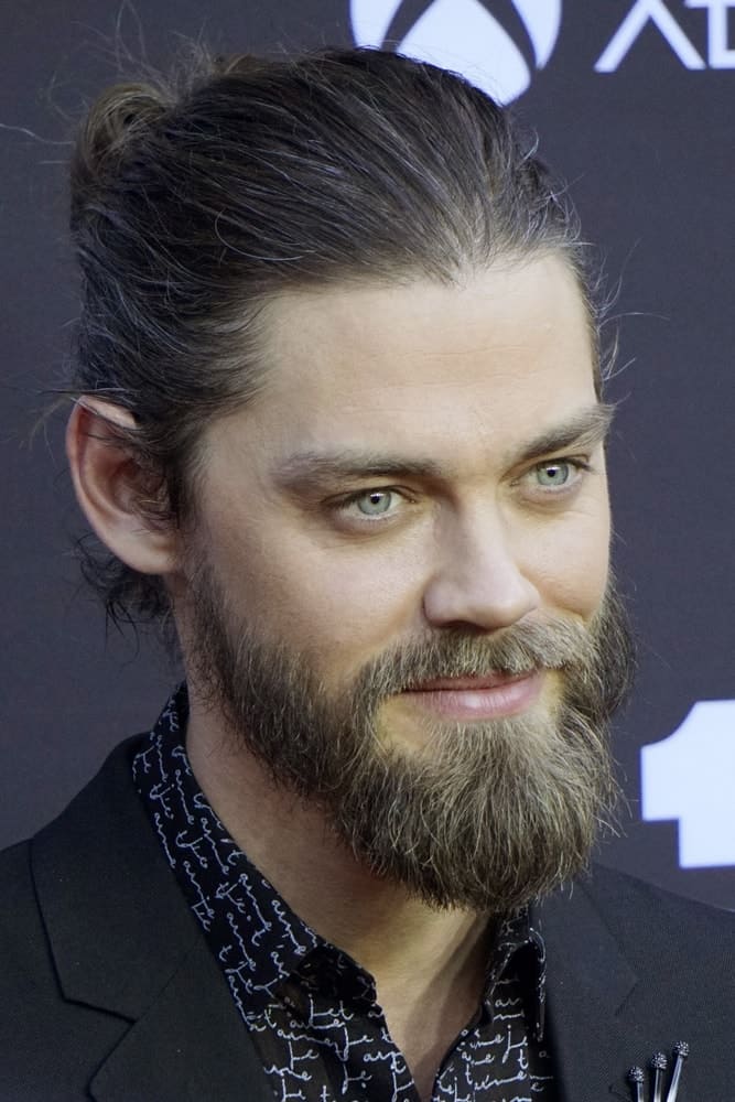 Tom Payne during October 22, 2017 at the "The Walking Dead" 100th Episode Celebration, with full beard and a man bun hairstyle.