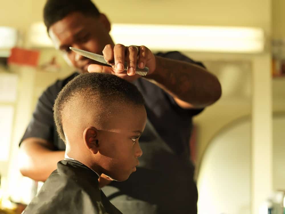 A little kid having his hair cut by a barber.