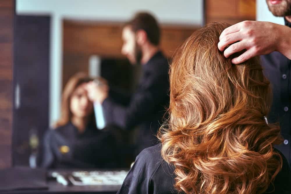 A stylist working on a woman's long wavy hair.