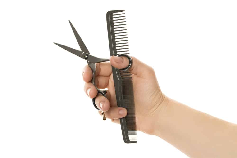A pair of scissors and a comb held in hand.