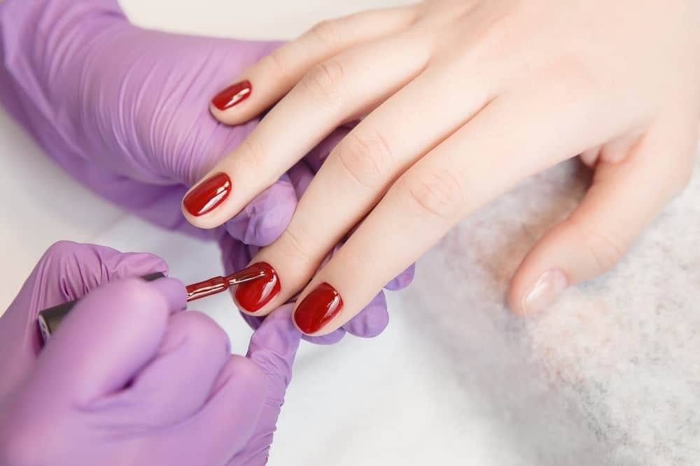 A woman having her nails done in a salon with a red finish.