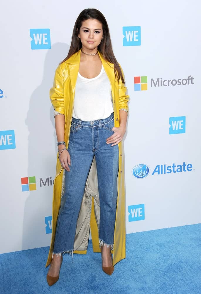 Selena Gomez attended the WE Day California held at the Forum in Inglewood, USA on April 7, 2016. She paired her casual clothes with a yellow trench coat and a long straight dark hairstyle.