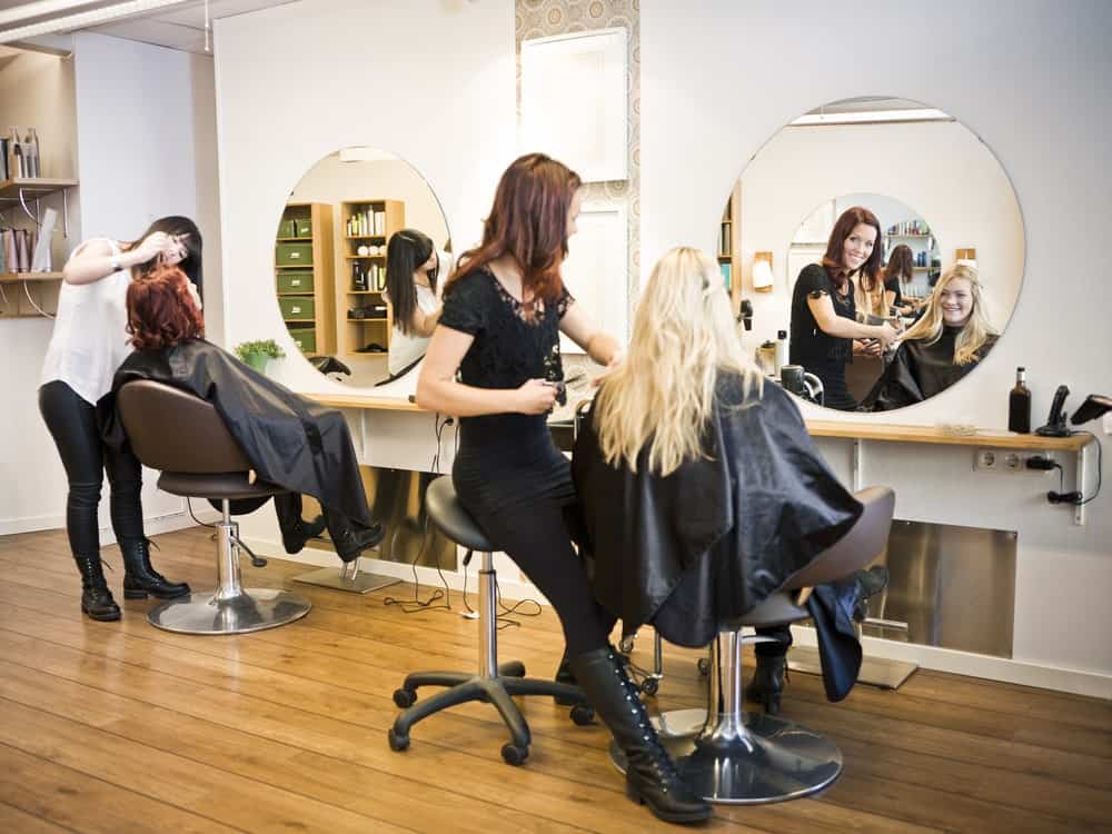 Two women getting a haircut in a beautiful modern salon with wooden flooring.