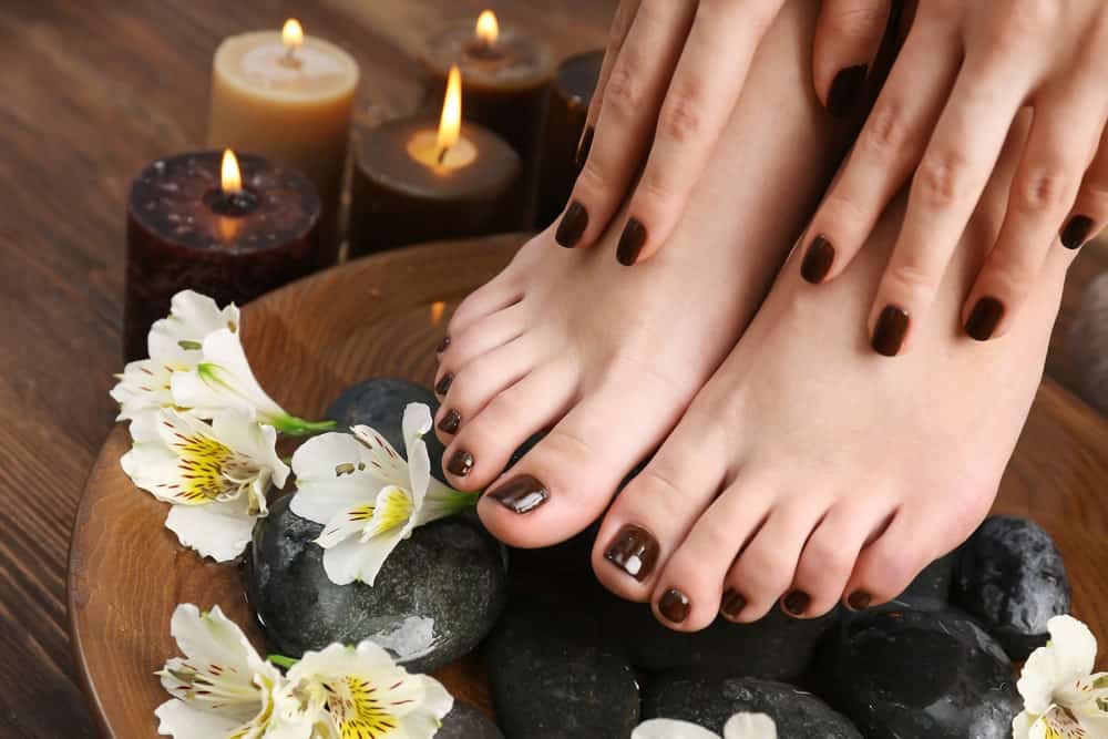 Manicured female feet and hands in spa wooden bowl with flowers and water.