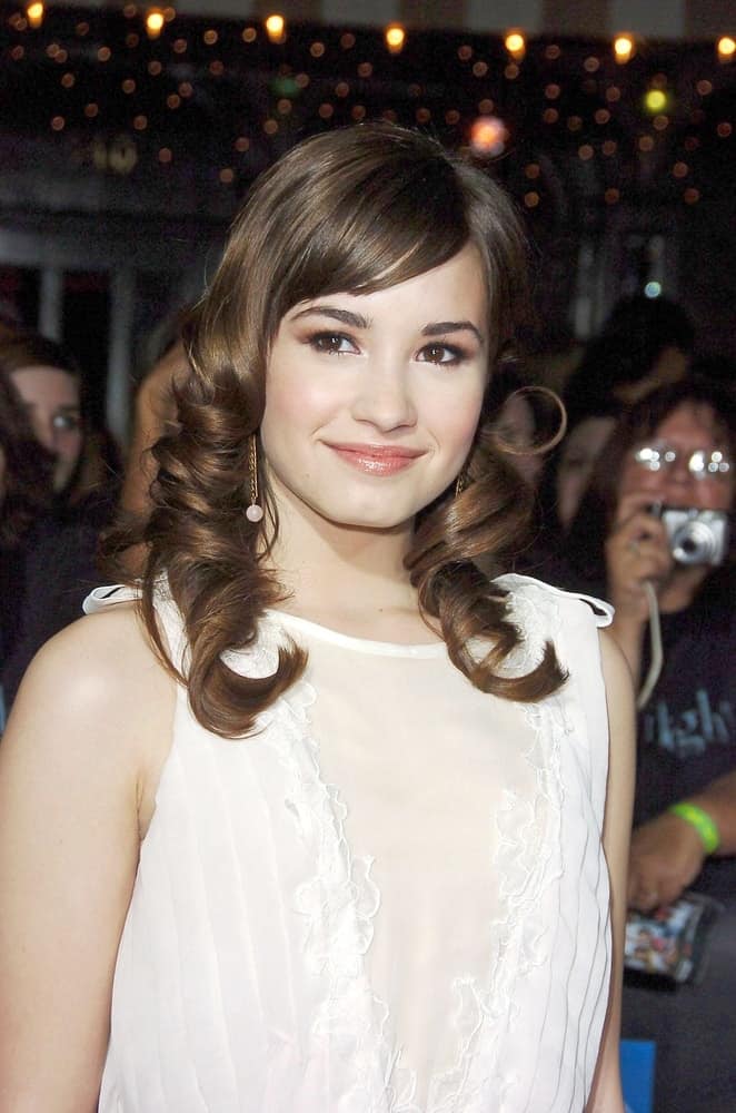 The young actress Demi Lovato was at the TWILIGHT Premiere held at the Mann Village and Bruin Theaters in Los Angeles, CA on November 17, 2008. She wore a simple white dress with her medium-length curly highlighted hairstyle with bangs.
