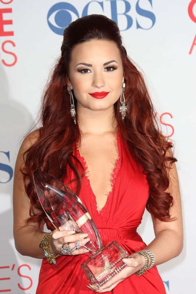 Demi Lovato was quite stunning with her red dress, red lips and red-dyed hairstyle in a half-up tousled hairstyle with waves and curls at the 2012 People’s Choice Awards Press Room, Nokia Theatre in Los Angeles, CA on January 11, 2012.