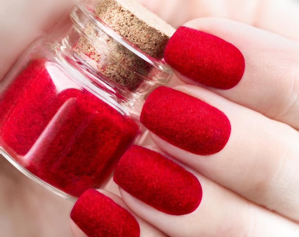 A close-up of trendy red velvet nails holding a bottle of red velvet polish.