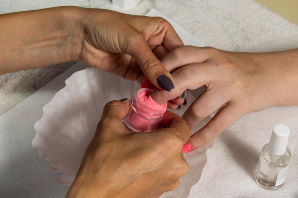 A manicurist using dip powder for a client's manicure.
