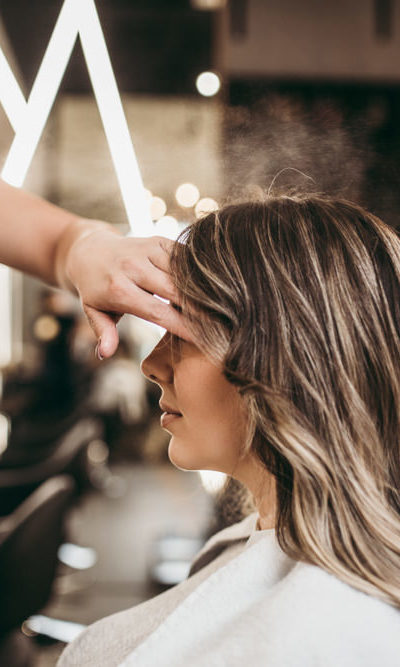 Hair stylist applying hair spray to woman