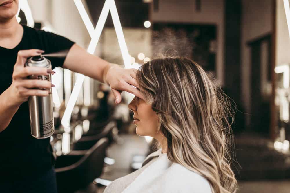 Hair stylist applying hair spray to woman