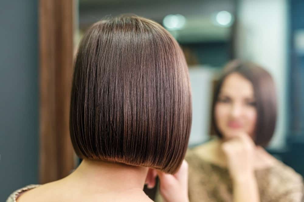 A woman with a plain bob hairstyle looking at herself in the mirror.