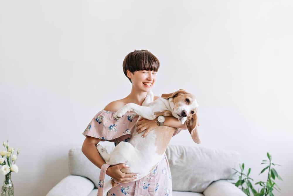 A woman with a bowl cut hairstyle carrying a dog.