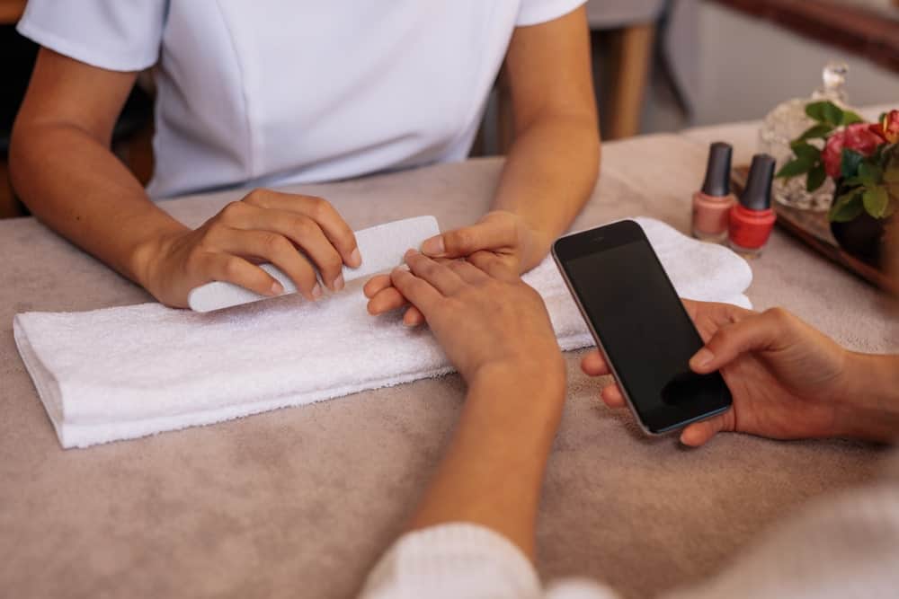 Cropped image of a person's hands holding a smartphone while getting a manicure.