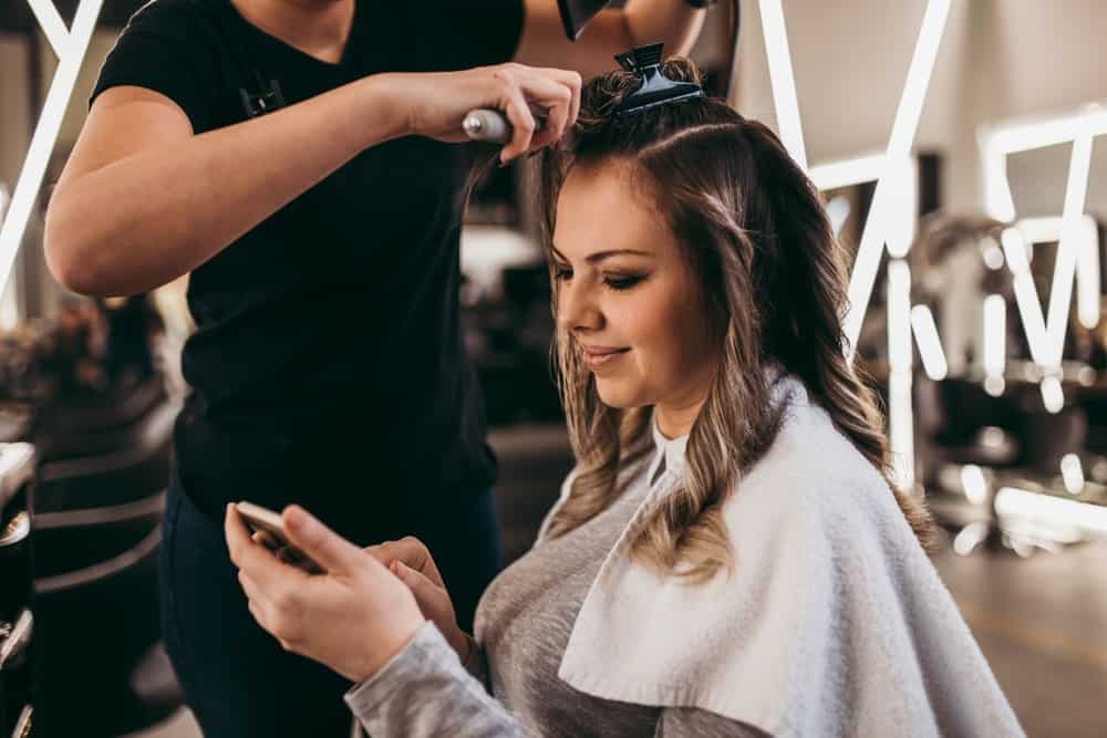 Woman checks her phone while a hairdresser works on her hair.