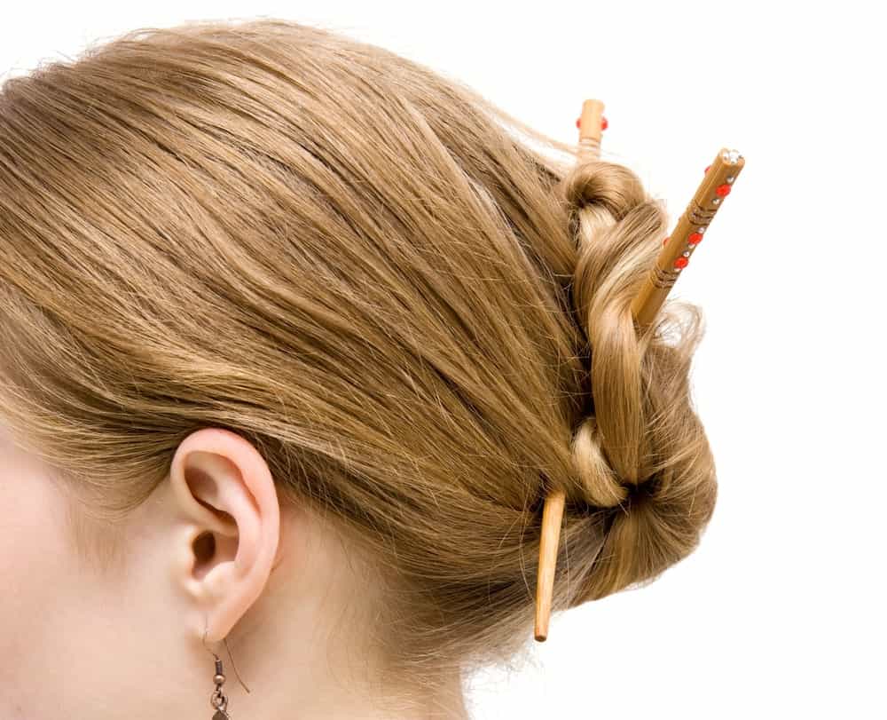 Side profile of a woman's head with her hair tied with chopsticks.