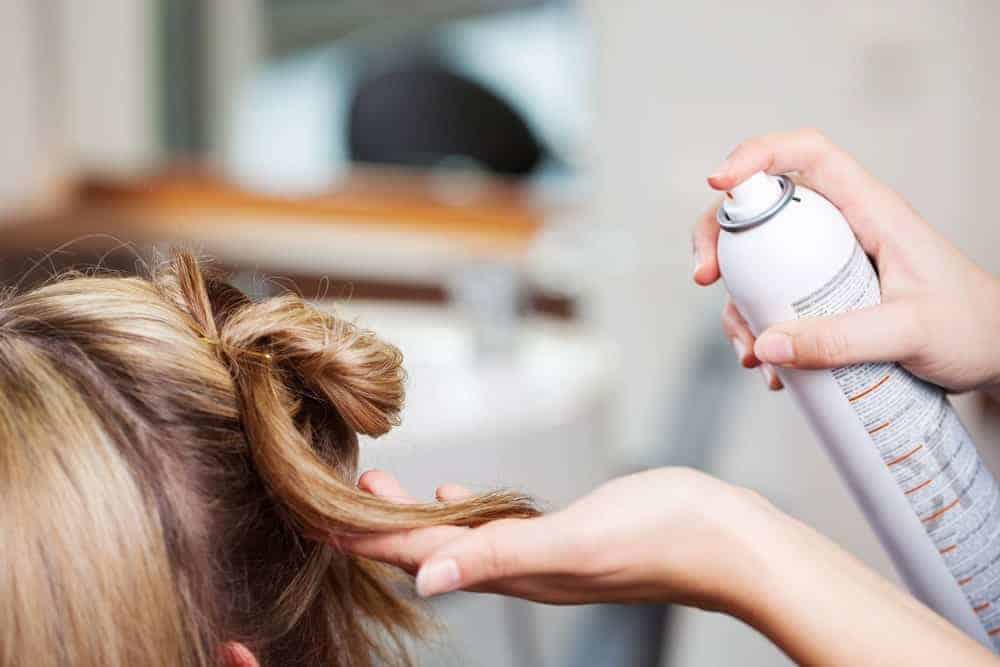 Hairstylist dispensing a hair spray on a woman's blonde hair.