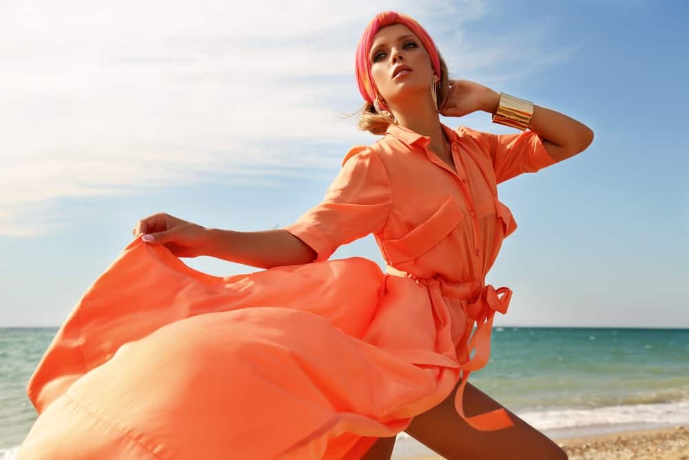 Woman in an orange dress and a matching hair scarf on the beach.