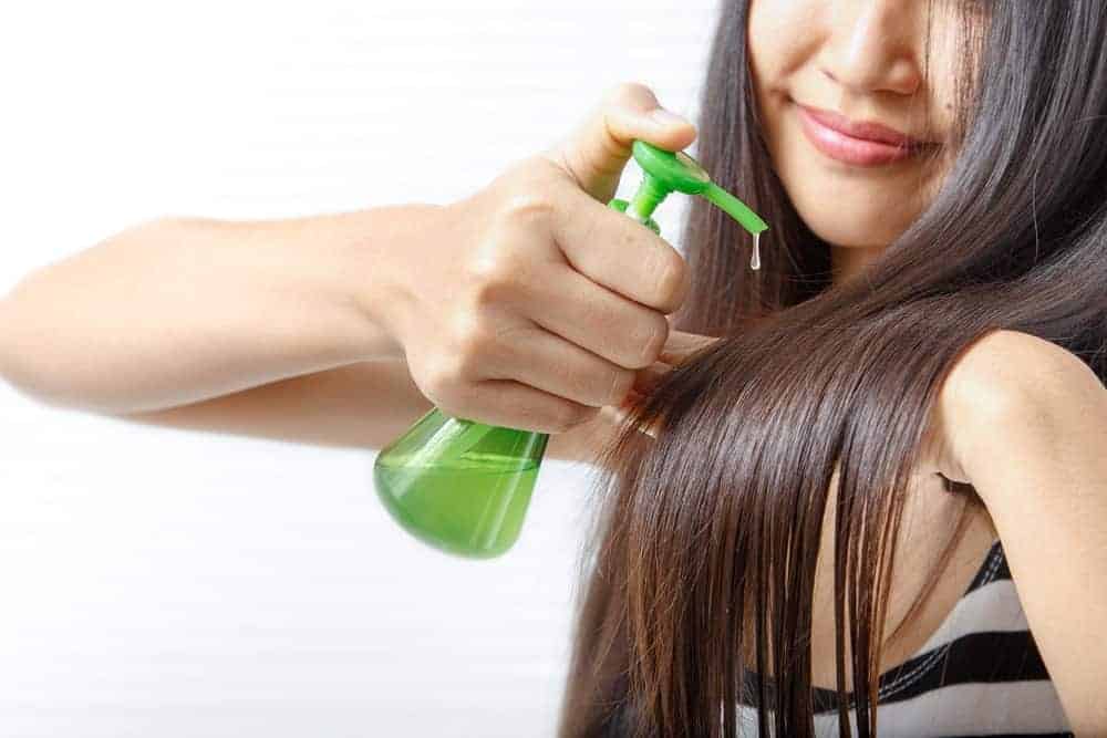 A woman pumping some hair oil into her long, straight hair.