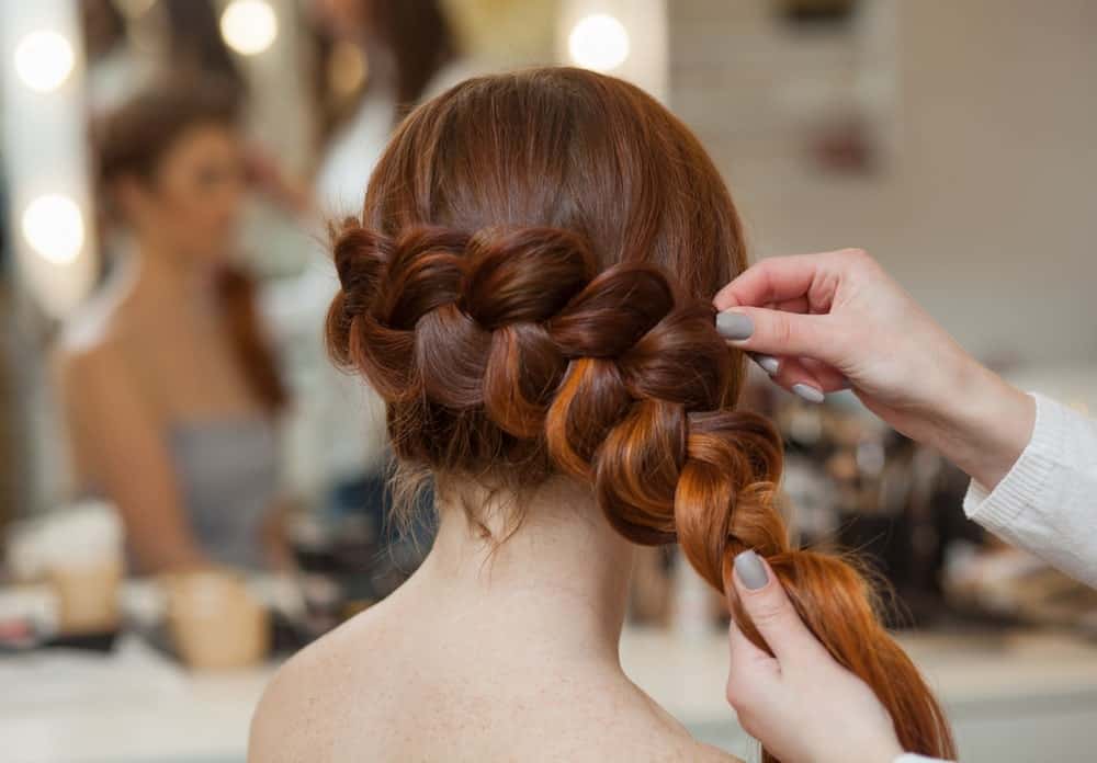 Professional hairdresser styling the woman's red hair in a side braid.
