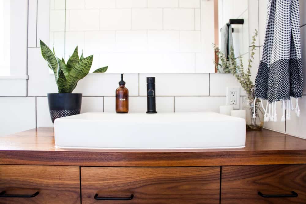 Wooden vanity topped with a vessel porcelain sink and a small potted plant.