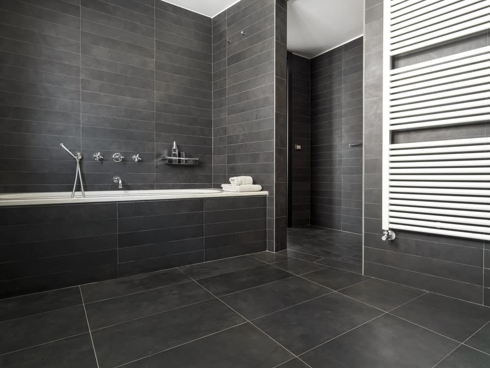 Modern bathroom with a drop-in bathtub clad in gray tiles that match the walls and flooring.